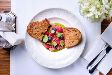 Tuna tartare with raspberries and blueberries in a white plate.