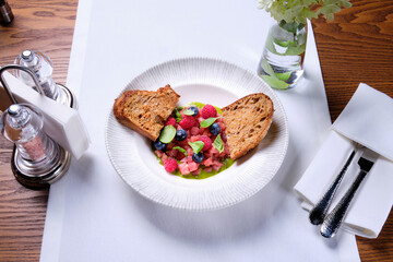 Tuna tartare with raspberries and blueberries in a white plate.