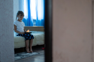Portrait of cutie little girl playing on digital tablet while sitting at home in living room.