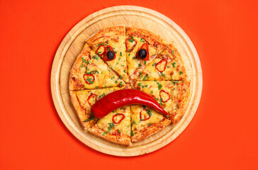 Delicious and appetizing pizza in the form of a sad emoji made of vegetables. Olives, peppers, cheese, sauce, chicken, salami, greens. View from above