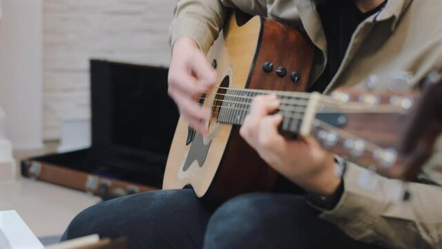 chico joven ensayando la guitarra mientras esta sentado en salon luminoso en un moderno apartamento