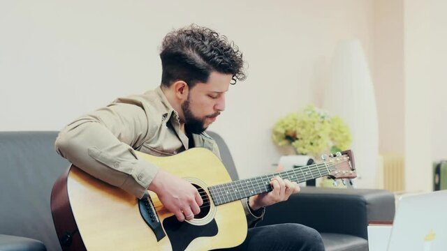 chico joven ensayando la guitarra mientras esta sentado en salon luminoso en un moderno apartamento