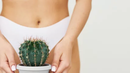 Abwaschbare Fototapete Depilation in the bikini zone concept. Woman holds cactus in pot on white panties background, epilation concept, intimate hygiene. Web banner © etonastenka