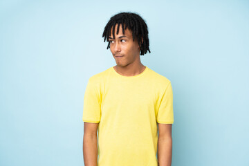 Young african american man isolated on blue background making doubts gesture looking side