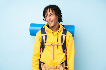 Young mountaineer african american man with a big backpack isolated on a blue background laughing...