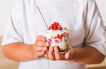 Layered trifle dessert with sponge cake, whipped cream and raspberries in child hands