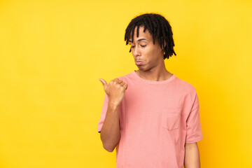 Young african american man isolated on yellow background unhappy and pointing to the side