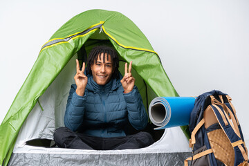 Young african american man inside a camping green tent showing victory sign with both hands