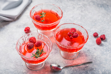 Raspberry jelly garnished with fresh raspberries and thyme on a light background.