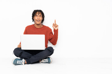 Young african american man sitting on the floor and working with his laptop pointing up and...