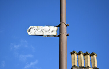 Old Metal 'Toilet's' Sign on Metal Lamp Post seen from below against Blue Sky 