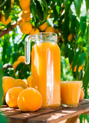 still life of ripe appetizing yellow peaches and jug of freshly squeezed peach juice on table in garden