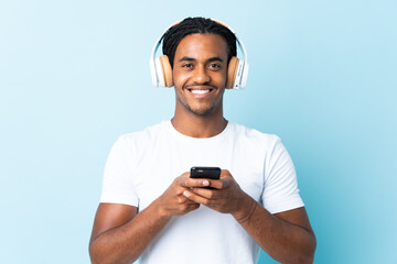 Young African American man with braids isolated on blue background listening music with a mobile and looking front