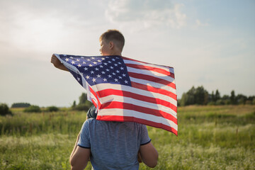 Little boy lets the american flag fly in his hands on the wind at the green field. Patriotic family...