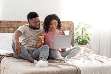 Black couple shopaholics making purchases online, using laptop