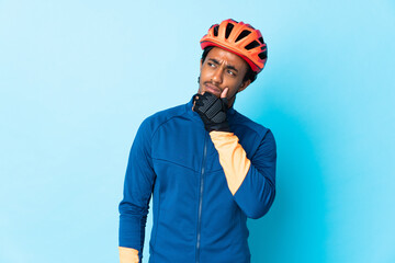 Young cyclist man with braids over isolated background having doubts