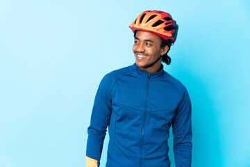 Young cyclist man with braids over isolated background looking to the side and smiling