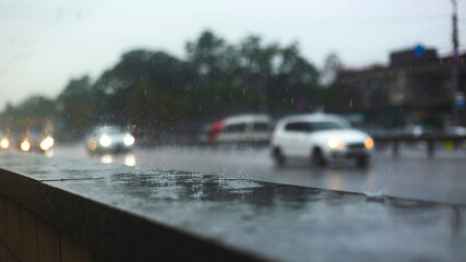 Urban rainy landscape. Drops on parapet along a busy road with cars