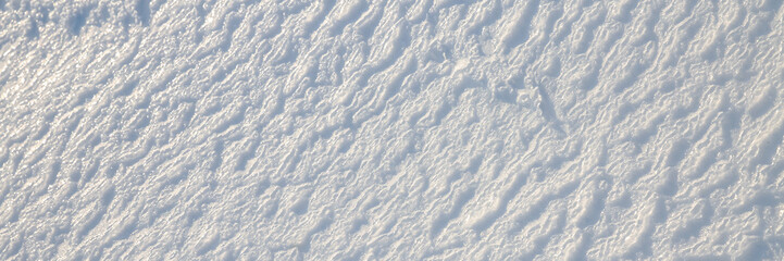 Beautiful winter background with snowy ground. Natural snow texture. Wind sculpted patterns on snow surface. Wide panoramic texture for background and design.