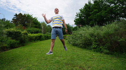 Strong young man in white t-shirt jumping on lawn in park