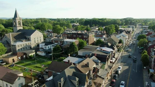 Aerial establishing shot of traditional American town city community, homes and church line street with traffic on road during summer magic hour light
