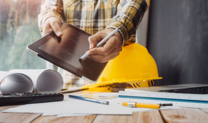 Two colleagues discussing data working and tablet, laptop with on on architectural project at construction site at desk in office