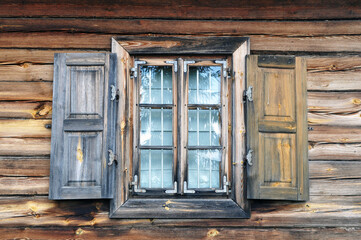 Naklejka na ściany i meble A shuttered window in an old country house. House walls made of natural timber with a window.