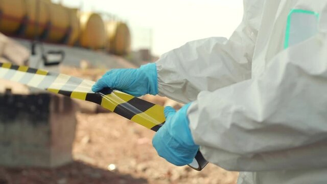 Pan shot of scientists wearing chemical repellant suits cordoning off the territory where eco-catastrophe has happened. Scientist rolling out danger restriction tape