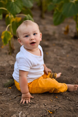 a happy baby sits on the ground in a field and smiles