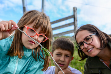 Happy family enjoying life together at meadow outdoor and observe Beautiful green grasshopper.