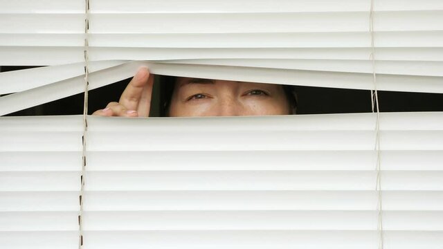 woman is watching someone through the blinds.
