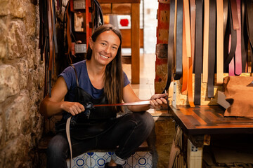 Fototapeta na wymiar Portrait of a female leather artisan in her workshop with hand-made belt