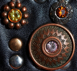 Macro shot of a "Bohemian" style fake leather belt with decorations, showing  a copper bead, leather texture and other beads in soft focus.