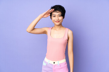 Young Vietnamese woman with short hair over isolated purple background saluting with hand with happy expression © luismolinero