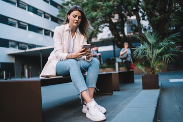 Beautiful hipster girl in electronic headphones listening received audio message using 4g wireless for network chatting during leisure in city, Caucasian blogger in earphones watching video vlog