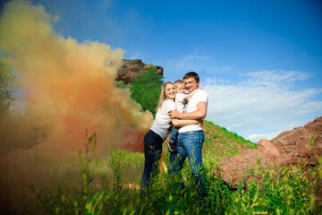 Happy family of three on a background of colored smoke in summer