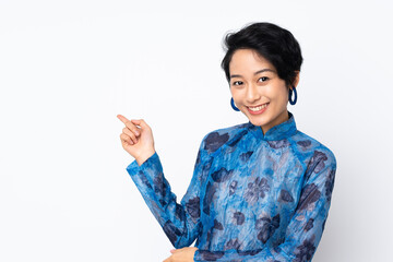 Young Vietnamese woman with short hair wearing a traditional dress over isolated white background pointing finger to the side