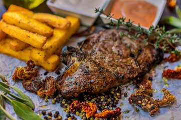 Delicious piece of meat served with potatoes decorated with dry tomatoes, pepper and herbs