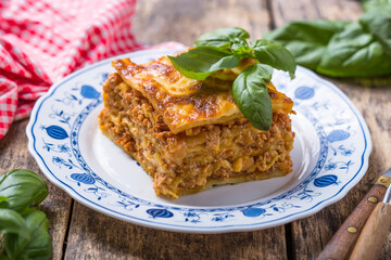 Meat lasagna with fresh basil and parmesan cheese in a plate on wooden table. close up. italian food.