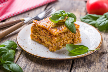 Meat lasagna with fresh basil and parmesan cheese in a plate on wooden table. close up. italian food.