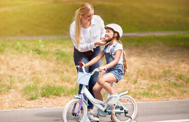 Mother Teaching Daughter To Ride A Bicycle Outdoor In Park