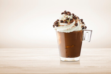 Cup of coffee with whipped cream, cocoa powder and chocolate chips on wooden table.