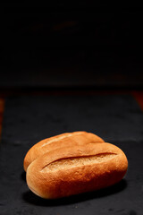 Freshly made plain bread bun on black stone cutting board. Very shallow depth of field
