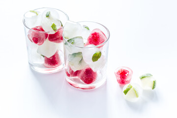 Cocktail glasses with berries in ice cubes on white table