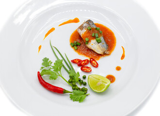 Sardine piece in tomato sauce decorated by chili ,spring onion , pepper , coriander and lemon in the white plate.