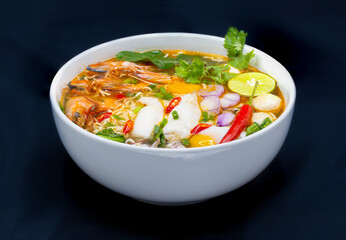 Tom Yum Kung, Thailand favorite spicy boiled food with ingredient are prawn, squid, fish, egg, meat ball and many spicy Thai herb, ready to serve in white bowl on dark background.