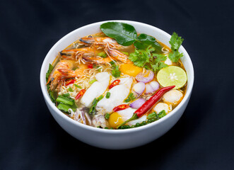 Tom Yum Kung, Thailand favorite spicy boiled food with ingredient are prawn, squid, fish, egg, meat ball and many spicy Thai herb, ready to serve in white bowl on dark background.