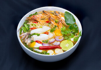 Tom Yum Kung, Thailand favorite spicy boiled food with ingredient are prawn, squid, fish, egg, meat ball and many spicy Thai herb, ready to serve in white bowl on dark background.