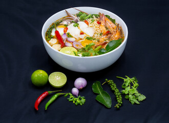 Tom Yum Kung, Thailand favorite spicy boiled food with ingredient are prawn, squid, fish, egg, meat ball and many spicy Thai herb, ready to serve in white bowl on dark background.