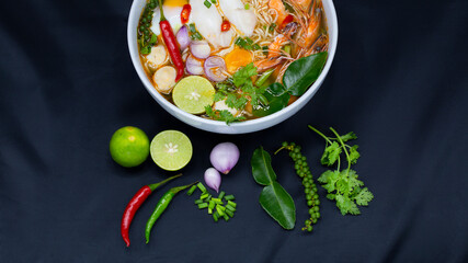 Tom Yum Kung, Thailand favorite spicy boiled food with ingredient are prawn, squid, fish, egg, meat ball and many spicy Thai herb, ready to serve in white bowl on dark background.